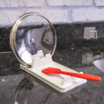 Weißer Topfdeckelhalter 2-in-1 mit rotem Pfannenwender und Glasdeckel auf Arbeitsplatte